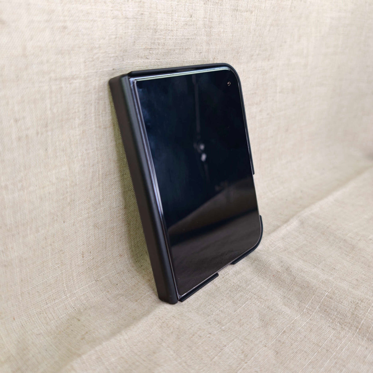 A black protective case for the iphone duo, shown in a partially folded position on a textured beige fabric background.